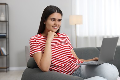 Photo of Happy young woman having video chat via laptop on sofa in living room