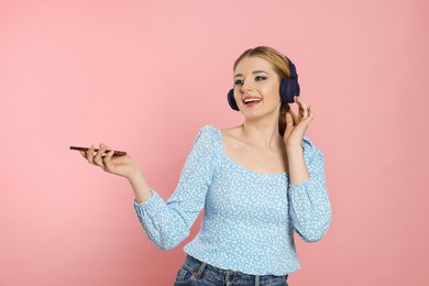 Photo of Happy woman in headphones enjoying music and holding smartphone on pink background