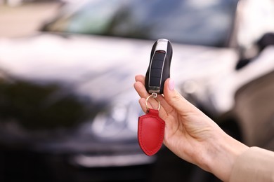 Woman holding car flip key near her vehicle outdoors, closeup