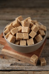 Photo of Brown sugar cubes in bowl on wooden table, closeup