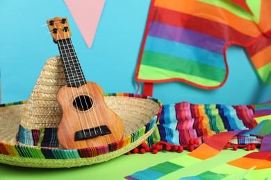 Photo of Mexican sombrero hat and ukulele on green table, closeup
