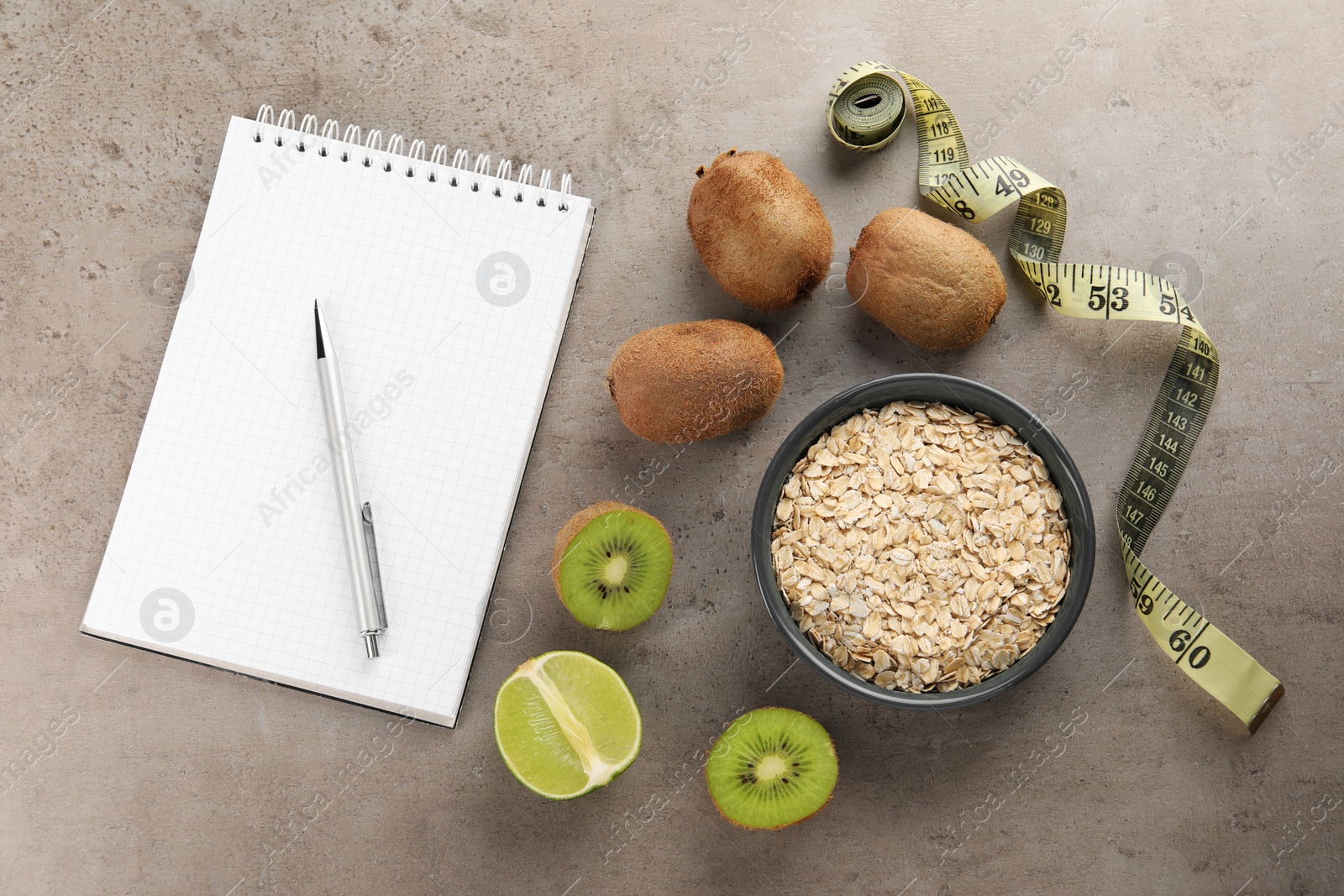 Photo of Healthy diet. Notebook, measuring tape, pen and products on grey table, flat lay