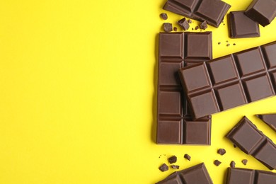 Photo of Pieces of delicious dark chocolate bars on yellow background, flat lay. Space for text