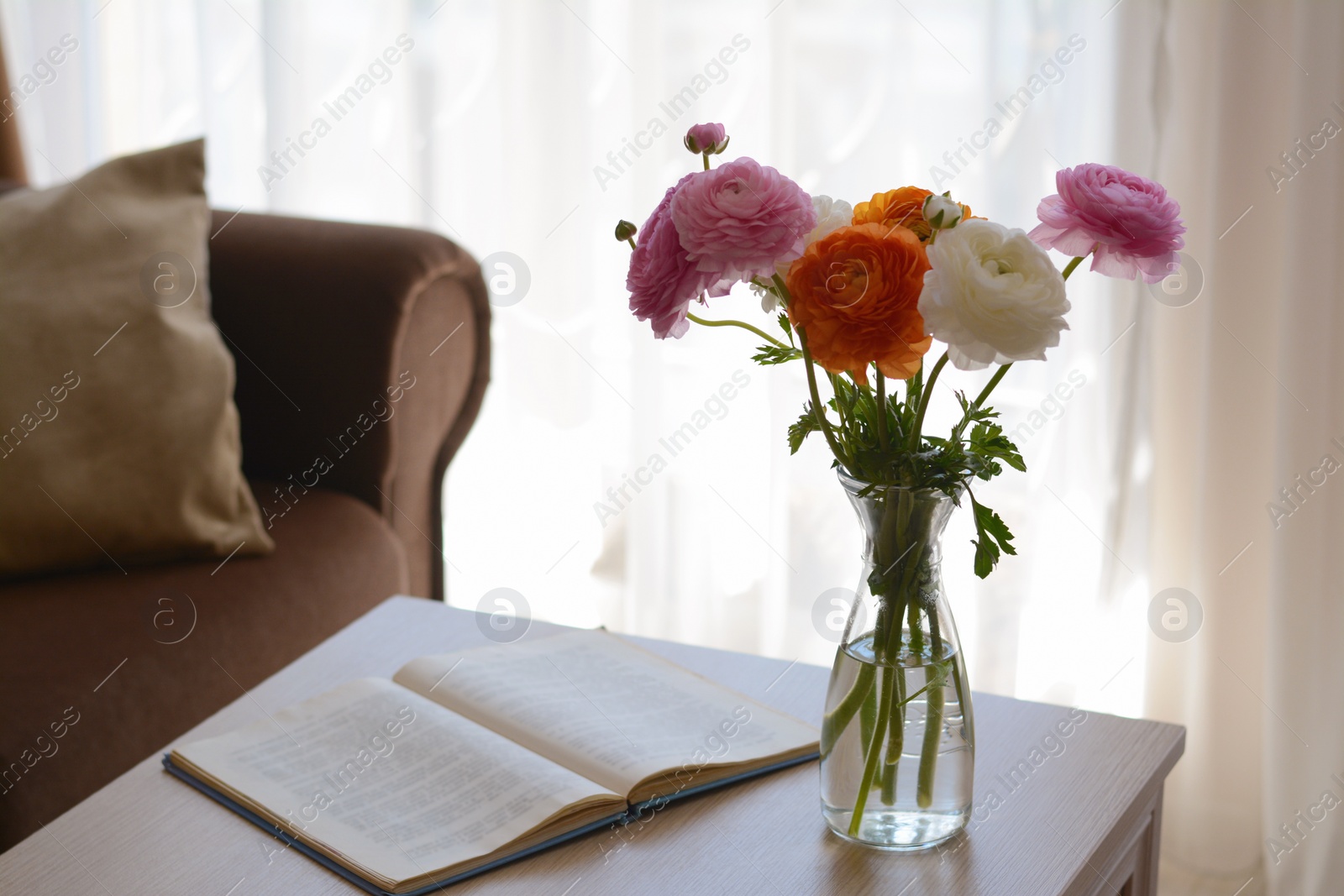 Photo of Bouquet of beautiful ranunculus flowers in vase and open book on wooden table indoors. Space for text