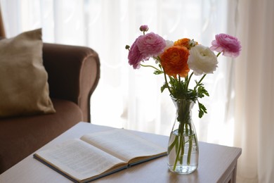 Bouquet of beautiful ranunculus flowers in vase and open book on wooden table indoors. Space for text