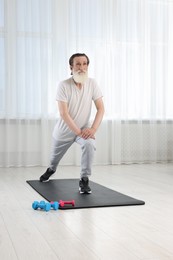 Photo of Senior man in sportswear stretching on fitness mat at home
