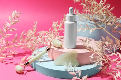 Photo of Beautiful composition with gua sha stone, face roller and bottle of serum on pink background
