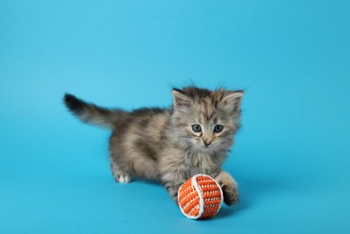 Photo of Cute kitten playing with ball on light blue background. Space for text