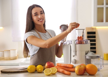 Young woman making tasty fresh juice at table in kitchen