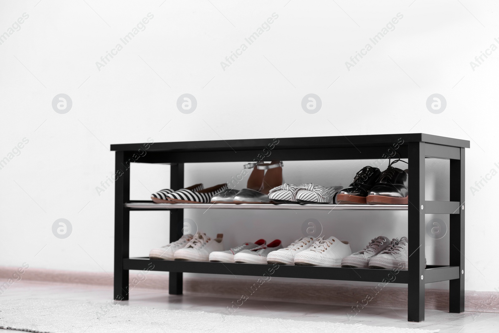 Photo of Shoe rack with different footwear near white wall. Stylish hallway interior