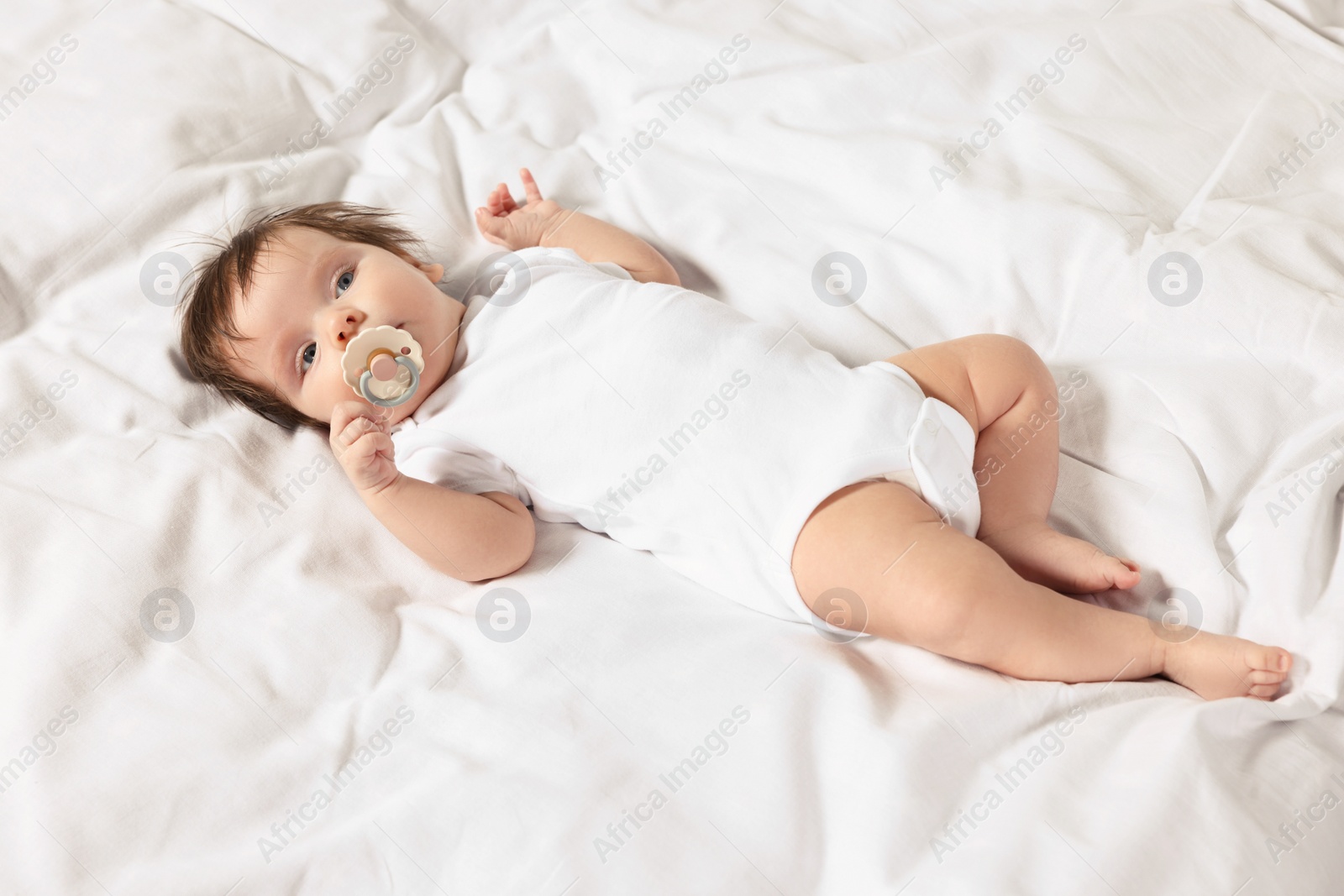 Photo of Cute little baby with pacifier lying on bed