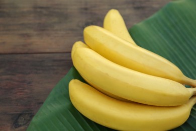 Delicious bananas and green leaf on wooden table, closeup. Space for text