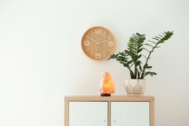 Himalayan salt lamp and plant on cabinet against white wall