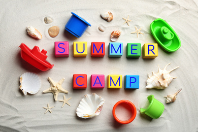Flat lay composition with phrase SUMMER CAMP made of colorful cubes on sand