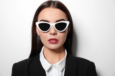 Photo of Young businesswoman in stylish sunglasses on light background
