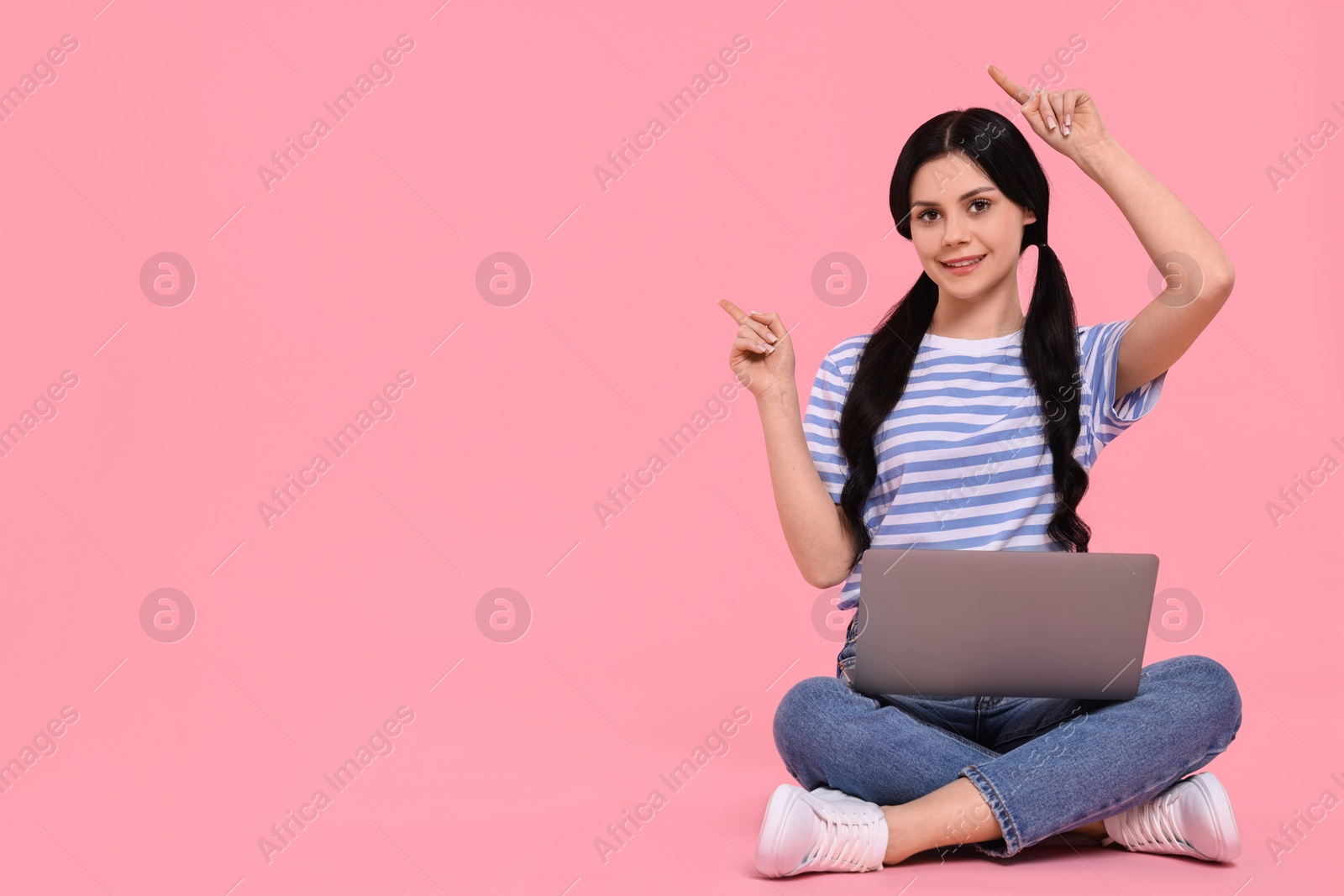 Photo of Smiling student with laptop pointing at something on pink background. Space for text