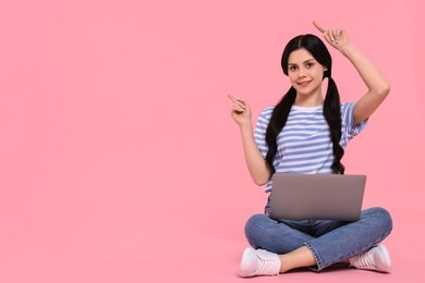 Smiling student with laptop pointing at something on pink background. Space for text