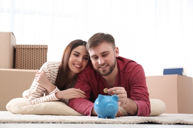 Photo of Beautiful young couple with piggy bank and money on floor at home