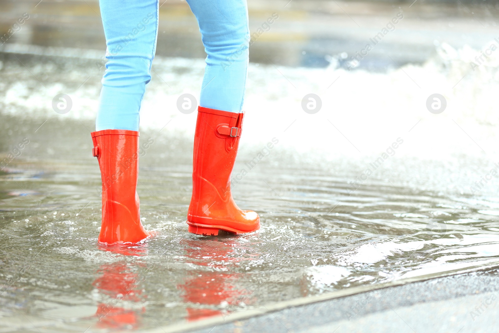 Photo of Woman with red rubber boots in puddle, closeup. Rainy weather