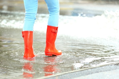 Woman with red rubber boots in puddle, closeup. Rainy weather