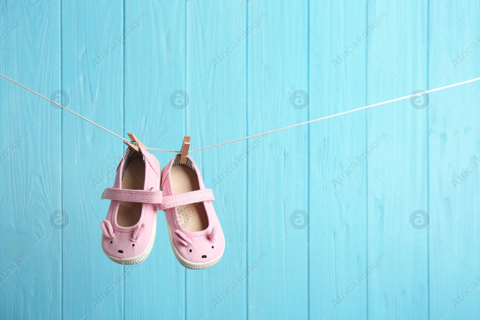 Photo of Baby shoes on laundry line against color wooden background, space for text. Child accessories