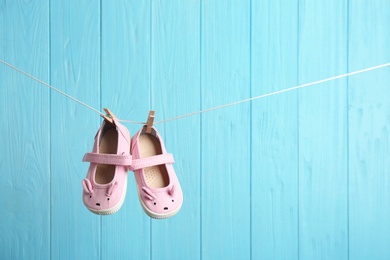 Baby shoes on laundry line against color wooden background, space for text. Child accessories