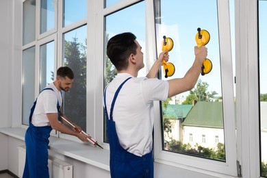 Photo of Workers with tube of sealant and suction lifters installing plastic windows indoors
