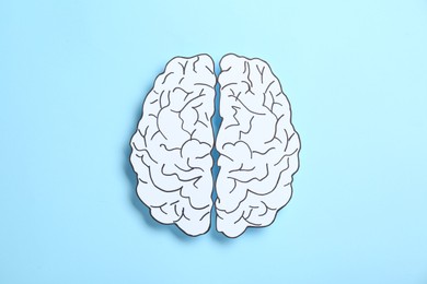 Paper brain hemispheres on light blue background, top view