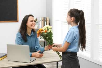 Schoolgirl congratulating her pedagogue with bouquet in classroom. Teacher's day