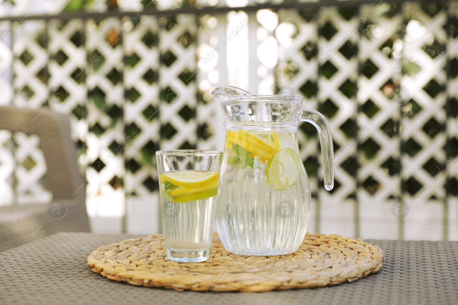 Photo of Glass and jug of water with lemons on table outdoors