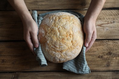 Photo of Man holding loaf of fresh bread at wooden table, top view