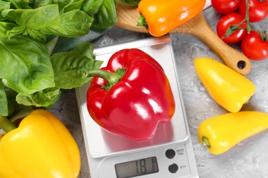 Kitchen scale with bell pepper among basil and tomatoes on grey textured table, flat lay