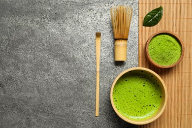 Photo of Cup of fresh matcha tea, bamboo whisk, spoon and green powder on grey table, flat lay. Space for text