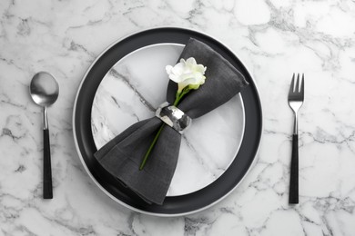 Stylish setting with cutlery, napkin, flowers and plates on white marble table, top view