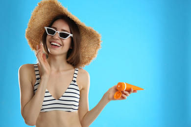 Young woman applying sun protection cream on light blue background. Space for text