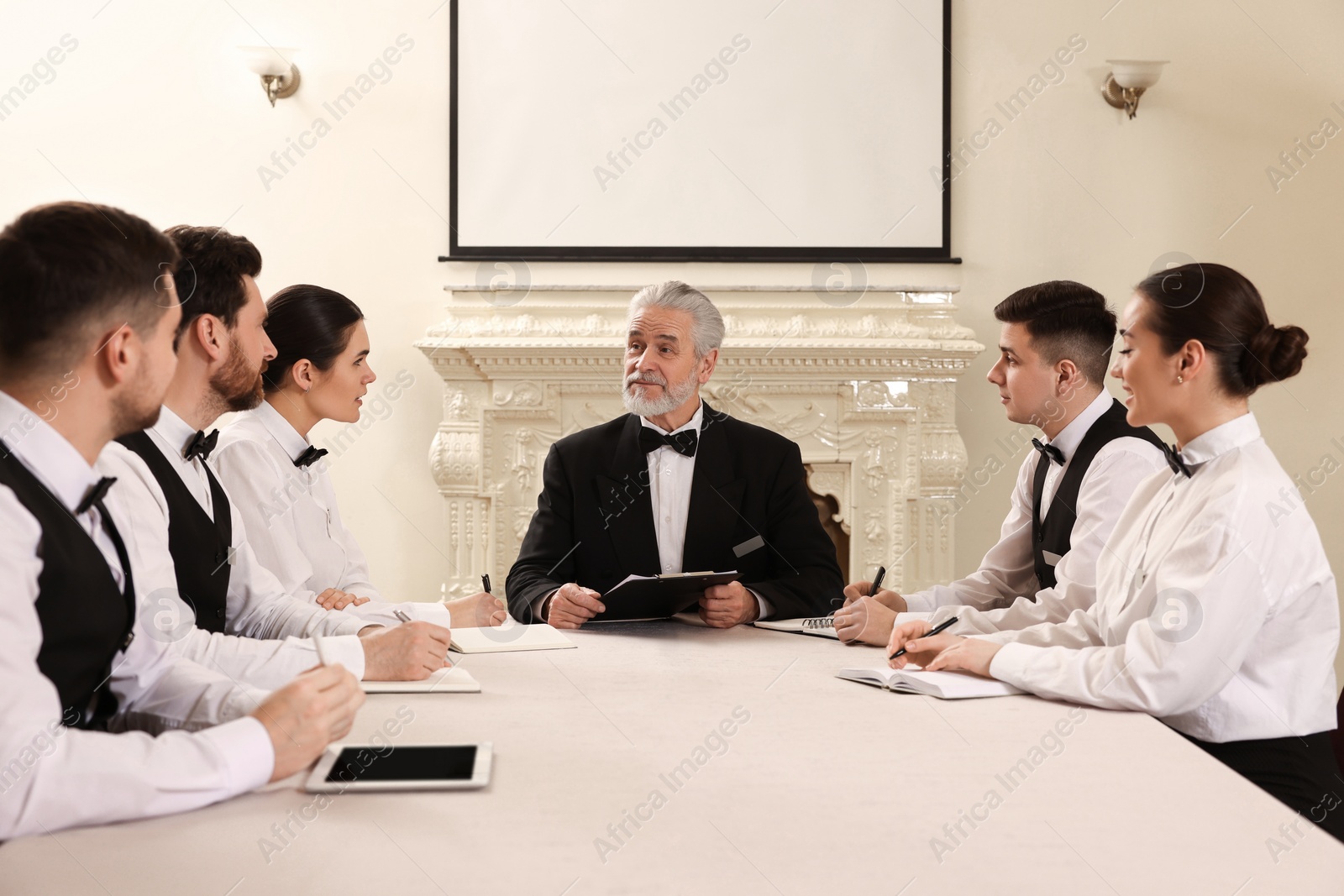 Photo of Senior man in formal suit teaching trainees indoors. Professional butler courses