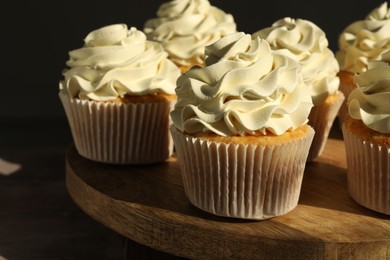 Photo of Tasty cupcakes with vanilla cream on wooden stand, closeup