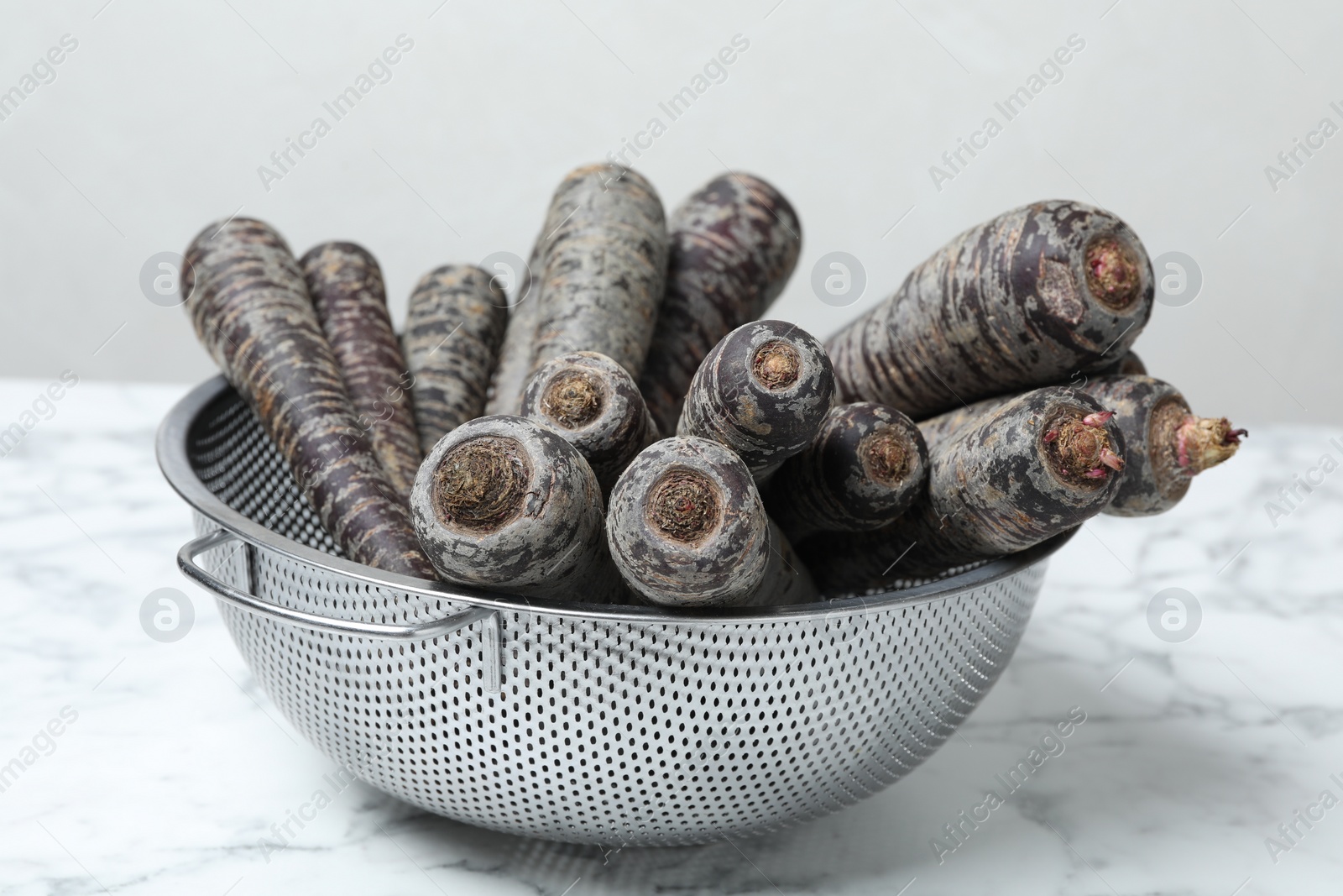 Photo of Raw black carrots in colander on white table