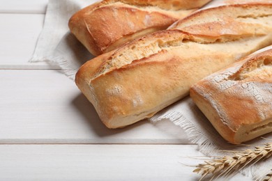 Photo of Tasty baguettes and spikelets on white wooden table, closeup