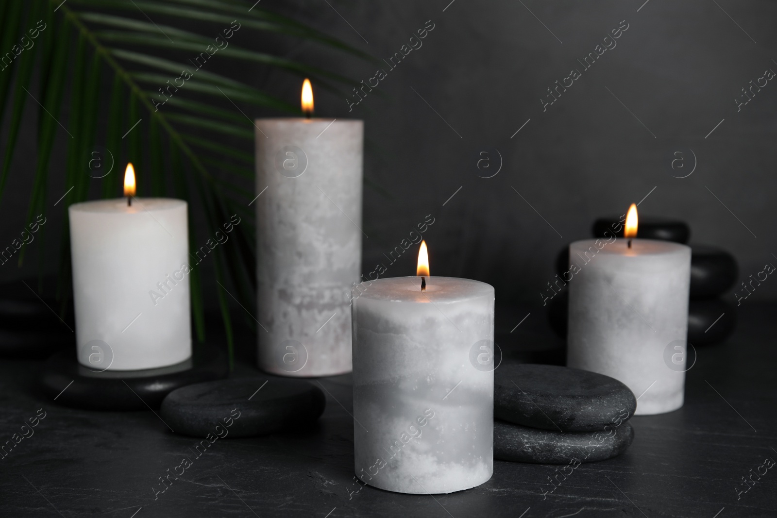 Photo of Burning candles and spa stones on black table