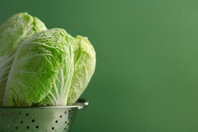 Photo of Fresh Chinese cabbages in colander on green background, closeup. Space for text