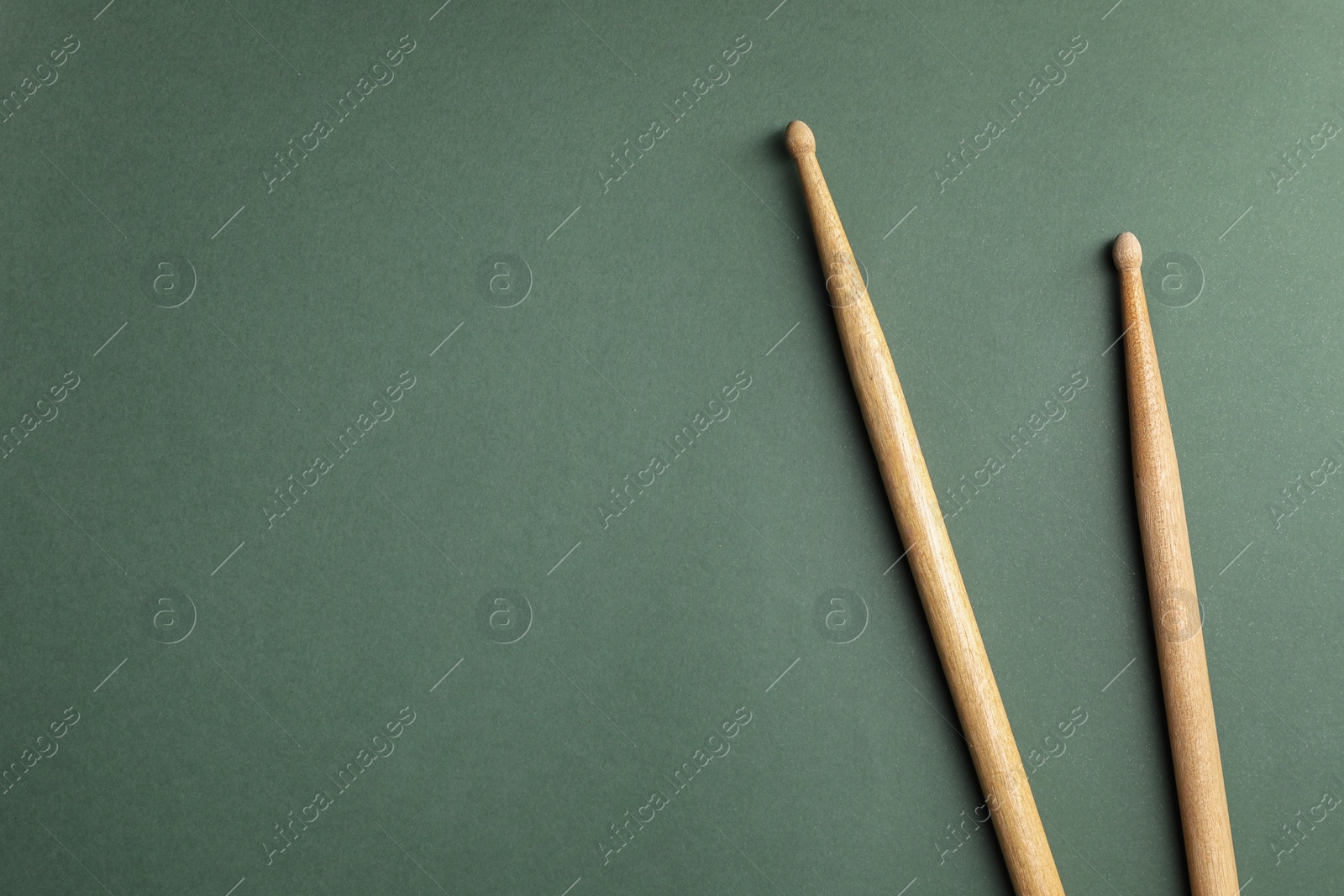 Photo of Two wooden drum sticks on olive background, top view. Space for text