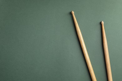 Photo of Two wooden drum sticks on olive background, top view. Space for text