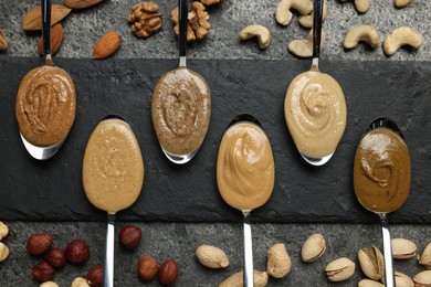Photo of Tasty nut butters in spoons and raw nuts on gray table, flat lay