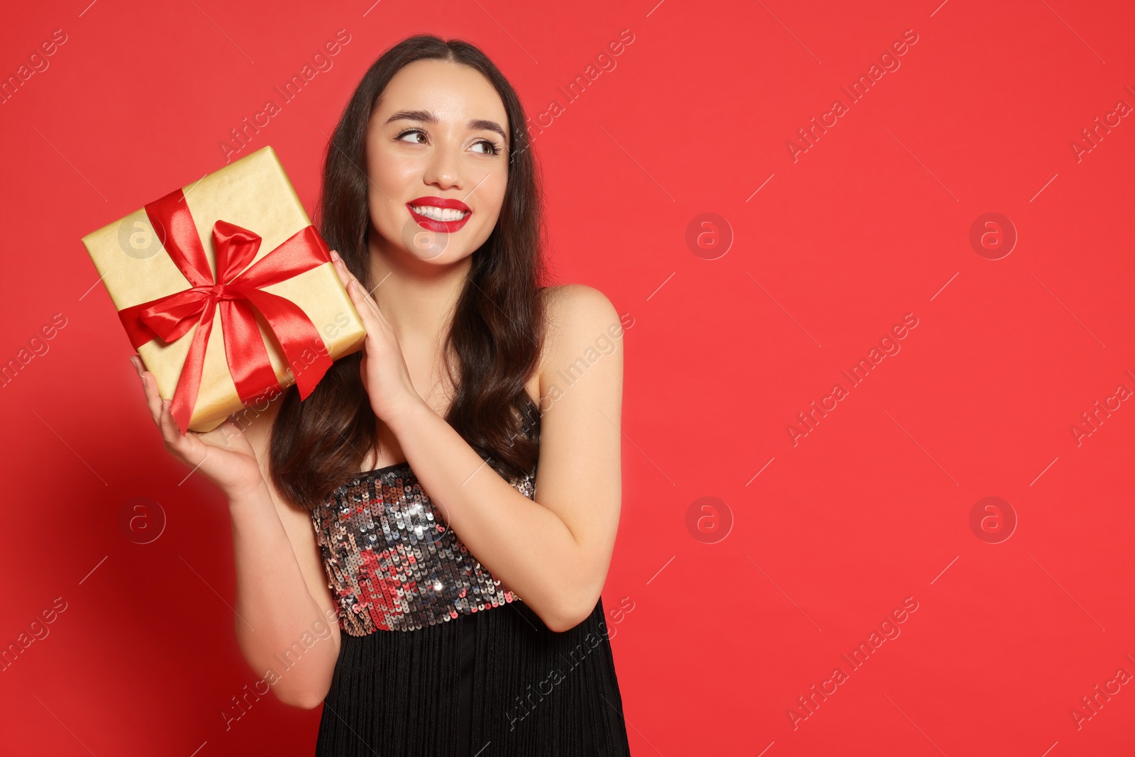 Photo of Beautiful young woman with Christmas gift on red background, space for text