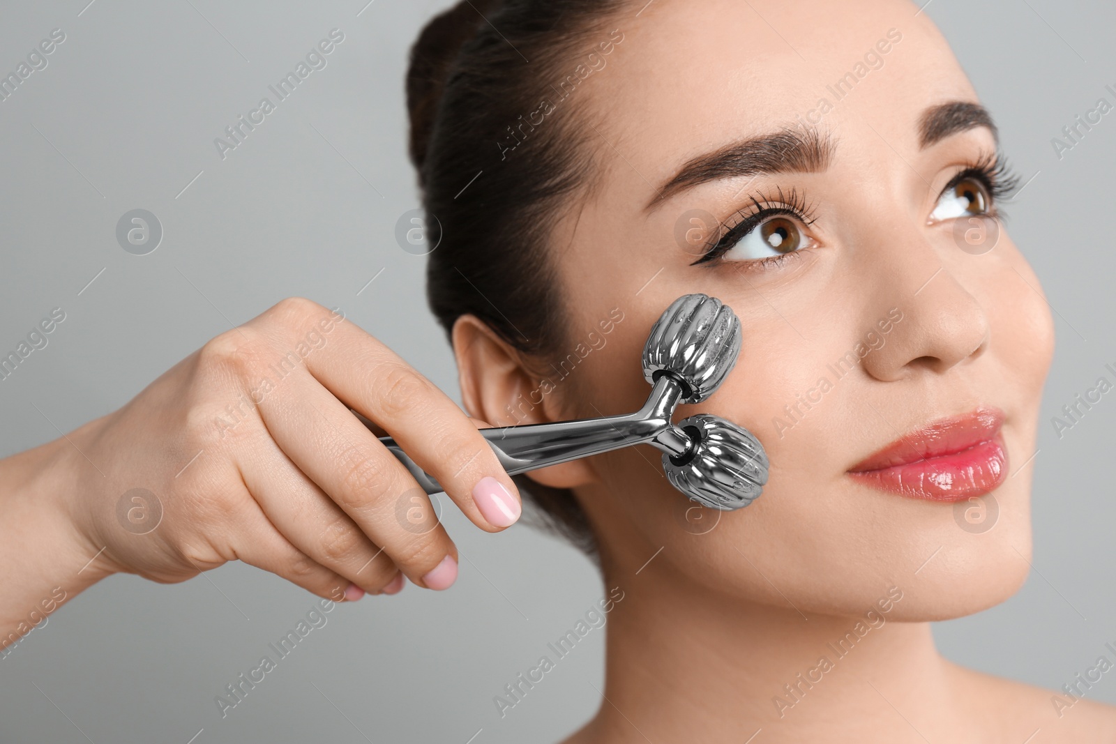 Photo of Woman using metal face roller on grey background, closeup