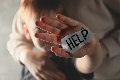 Photo of Little boy and mother holding piece of paper with word Help on hand against light grey background, closeup. Domestic violence concept