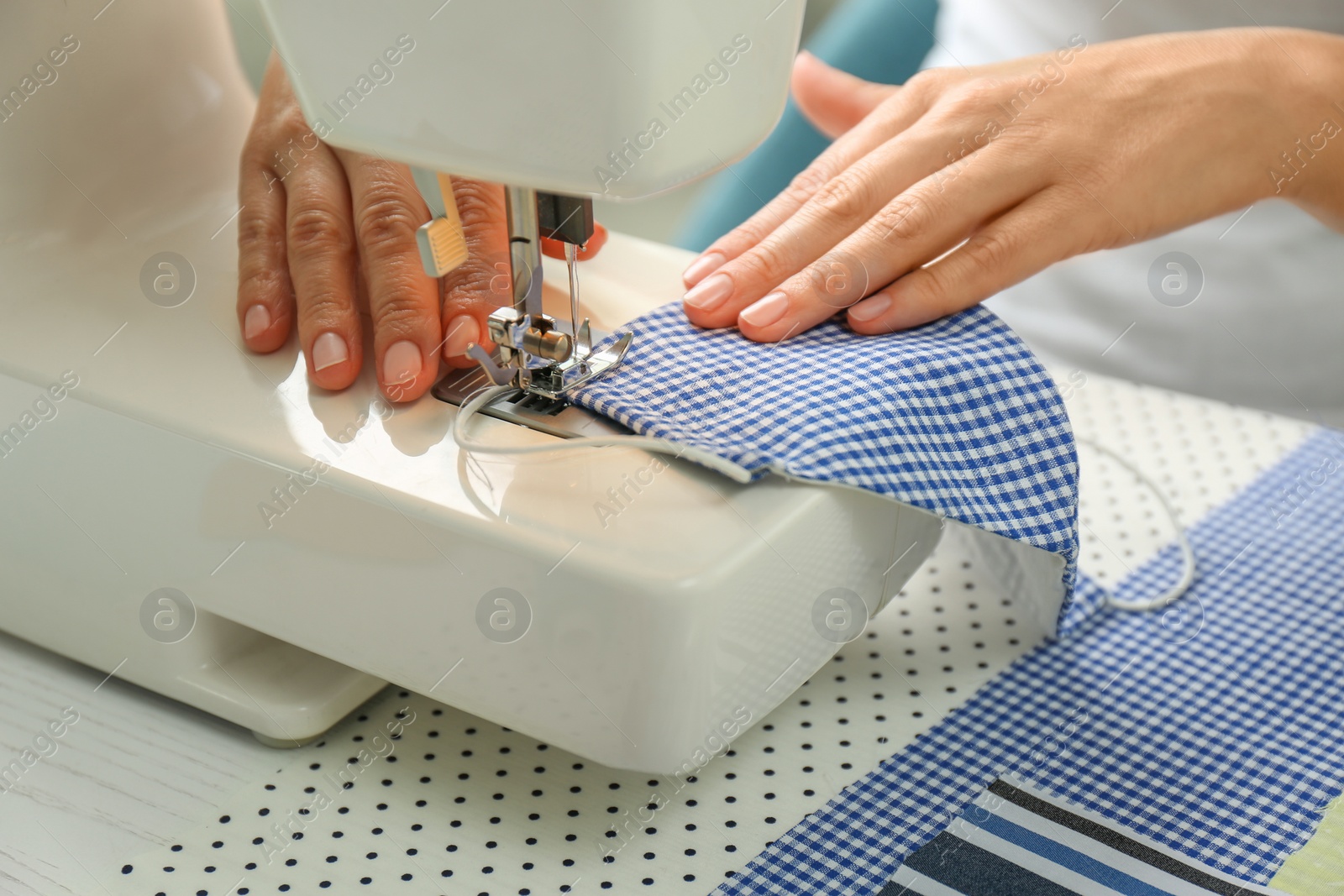 Photo of Woman sewing cloth mask with machine at table, closeup. Personal protective equipment during COVID-19 pandemic