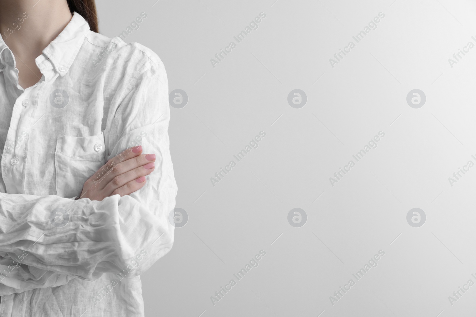 Photo of Woman wearing wrinkled white blouse on light grey background, closeup. Space for text