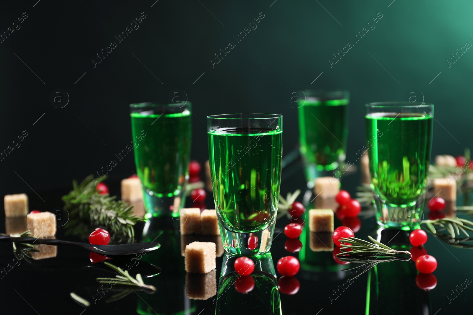 Photo of Absinthe in shot glasses, cranberries, rosemary and brown sugar on mirror table. Alcoholic drink